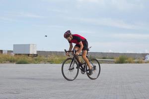 wielrenner in helm en sportkleding die alleen traint op een lege landweg, velden en bomenachtergrond foto