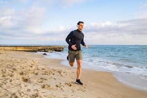 fit mannelijke hardloper training op het zomerstrand en luister naar muziek tegen prachtige lucht en zee foto