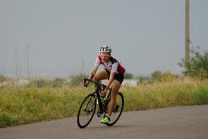 wielrenner in helm en sportkleding die alleen traint op een lege landweg, velden en bomenachtergrond foto