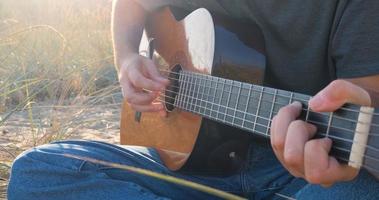 jonge knappe man speelt in akoestische gitaar op het strand in zonnige dag, zee of oceaan op de achtergrond foto