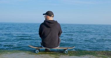 jonge man met skateboard ontspannen in de buurt van zee foto