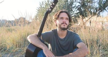 jonge knappe man speelt in akoestische gitaar op het strand in zonnige dag, zee of oceaan op de achtergrond foto