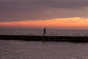 jonge man in herfstkleren trainen op het strand, zonsopgangachtergrond, mannelijke hardloper in de ochtend foto