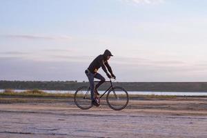 alleen rijder op fixed gear racefiets rijden in de woestijn in de buurt van rivier, hipster toeristische fietsrijder foto's. foto