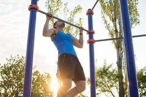gespierde man doet pull-ups op rekstok, training van sterke man op outdoor park gym in de ochtend. foto