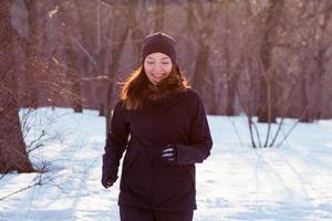 jonge vrouw atleet in zwarte sport pak rennen in winter park foto