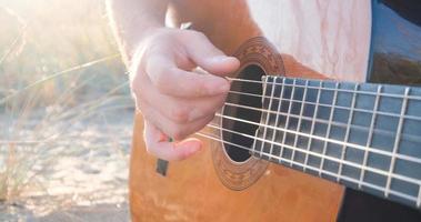 jonge knappe man speelt in akoestische gitaar op het strand in zonnige dag, zee of oceaan op de achtergrond foto