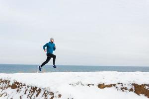 jonge mannelijke hardloper die in de winter buiten traint, man rent in de sneeuw foto