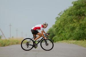 wielrenner in helm en sportkleding die alleen traint op een lege landweg, velden en bomenachtergrond foto