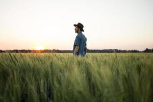 jonge mannelijke boer staat alleen in het tarweveld tijdens zonsondergang foto