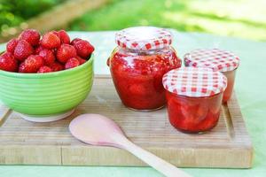 zelfgemaakte aardbeienjam in verschillende potten en verse rijpe aardbeien foto