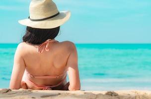 achteraanzicht van gelukkige jonge Aziatische vrouw in roze zwembroek en strohoed ontspannen en genieten van vakantie op tropisch paradijs strand bij zonsondergang. meisje in zomervakantie mode. schoonheid sexy model. elegante levensstijl foto