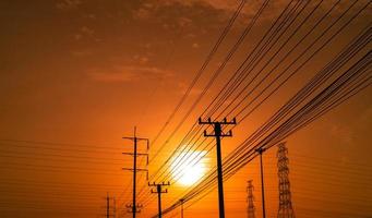 hoogspanning elektrische paal en transmissielijnen bij zonsondergang met oranje en rode lucht en wolken. architectuur. silhouet elektriciteitsmasten tijdens zonsondergang. kracht en energie. energiebehoud. foto