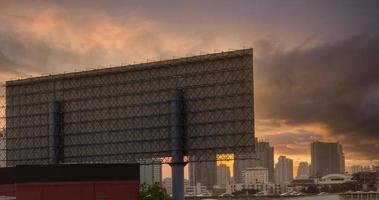 stadsgezicht. stad in de avond. weergave van achter de metalen structuur van billboard. hoogbouw kantoorgebouw en appartementencomplex in de hoofdstad met avondrood. auto rijden op de weg met verkeersopstopping foto