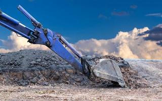 blauwe backhoe schop op de grond stenen weg met bewolkte hemel als achtergrond. foto