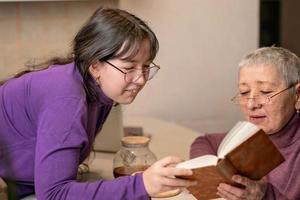 oma en kleindochter drinken thee aan tafel en lezen een boek. foto