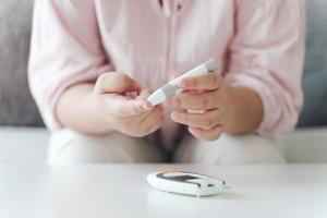 Aziatische vrouw die lancet op vinger gebruikt voor het controleren van de bloedsuikerspiegel door glucosemeter, gezondheidszorg en medisch, diabetes, glycemieconcept foto