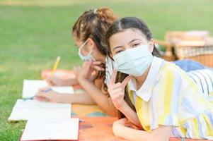 een half-Thais-Europees meisje en haar vriend dragen een antivirusmasker terwijl ze buiten school in een park leren foto