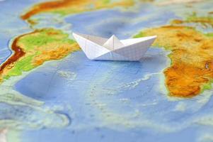 papieren boot op een achtergrondkaart van de wereld foto