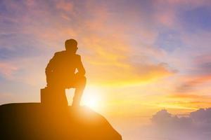 silhouet van zakenman geknield positie en kijken uit op een bergtop zonsondergang avond hemelachtergrond, succes en actief leven concept foto