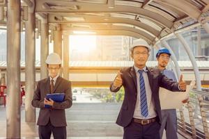 business team engineer schaven met witte helm en tekenpapier in de hand houden tegen stadsachtergrond schaven en teamwork management concept foto