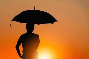 silhouet van een mooie vrouw met een paraplu op de zonsondergang achtergrond, gelukkig en geniet van het leven concept. foto