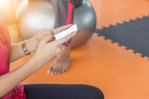 close-up van een jonge vrouw die haar smartphone gebruikt om te ontspannen na een fitnesstraining in de sportschool, technologie en een concept voor een gezonde, actieve levensstijl foto