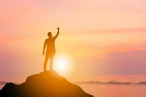 silhouet van man staande viering succes genieten op een bergtop tropische zonsondergang of zonsopgang strand achtergrond, geluk en actief leven concept. foto