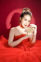 jonge Aziatische mooie vrouw model in een chique stijlvolle luxe rode jurk op een rode achtergrond geïsoleerd. foto