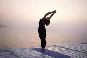 jonge vrouw poseren in yoga asans, ochtend zee achtergrond foto