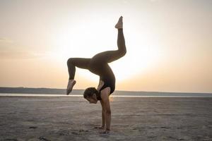 jonge fitte vrouw die yoga-houdingen traint in de woestijn tijdens de zonsondergang of zonsopgang, vrouw in zwarte sportkleding doet rekoefeningen foto