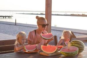 moeder met twee kinderen eet watermeloenplakken buiten in de zomer foto