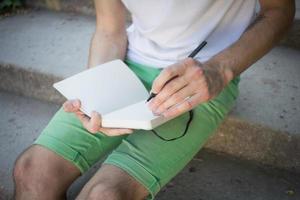 jonge man outddur in park schrijven in notitieboekje, student of schrijver op het werk foto