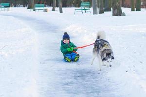 gelukkige jongen speelt met husky hond in winterpark vol sneeuw foto