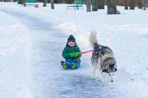 gelukkige jongen speelt met husky hond in winterpark vol sneeuw foto