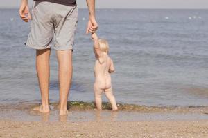 close-up foto van vader met een kind van een jaar dat 's zomers op het strand loopt