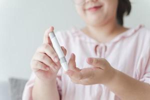 Aziatische vrouw die lancet op vinger gebruikt voor het controleren van de bloedsuikerspiegel door glucosemeter, gezondheidszorg en medisch, diabetes, glycemieconcept foto