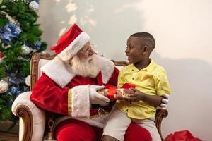 de kerstman levert een geschenkdoos aan een kleine Afrikaanse jongen. kerstavond, levering van geschenken. foto