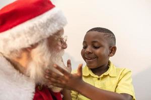 de kerstman levert een geschenkdoos aan een kleine Afrikaanse jongen. kerstavond, levering van geschenken. foto