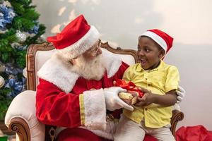 de kerstman levert een geschenkdoos aan een kleine Afrikaanse jongen. knuffel. kerstavond, levering van geschenken. foto