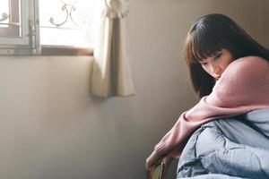 depressieve Aziatische tiener vrouw in slaapkamer dragen roze trui. foto