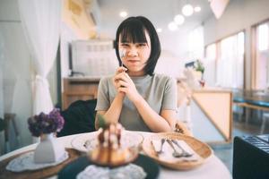 portret van gelukkige jonge volwassen Aziatische vrouw bij dessert café binnen op dag. foto