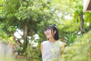 portret van jonge volwassen aziatische vrouw die een bril draagt en kort haar blijft thuis in de groene tuin op de dag. foto