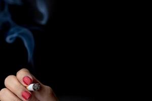 sigaret met rook in vrouw hand met rode nagel geïsoleerd op zwarte achtergrond met kopie ruimte voor tekst. vrouw roken. slechte gewoonte kan longkanker veroorzaken. gestresste vrouw met nicotineverslaafd concept foto