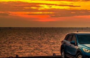 blauwe compacte suv-auto met sport en modern design geparkeerd op betonnen weg aan zee bij zonsondergang in de avond. hybride en elektrisch autotechnologieconcept. parkeerplaats. auto-industrie. foto