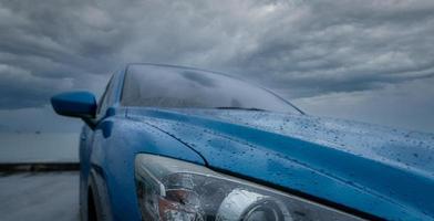 blauwe luxe suv-auto met waterdruppels geparkeerd op de weg naast zeestrand op regenachtige dag met stormhemel. regendruppels op blauwe suv-auto. roadtrip reizen. ev auto concept. electrisch voertuig. rij veilig na regen. foto