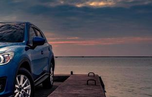 blauwe compacte suv-auto met sport en modern design geparkeerd op betonnen weg aan zee bij zonsondergang in de avond. hybride en elektrisch autotechnologieconcept. parkeerplaats. auto-industrie. foto