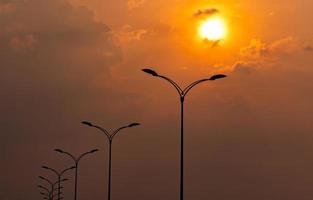 silhouet straat elektrische paal met prachtige oranje en gele avondrood en wolken in de avond. straatlantaarn licht. stadsweglantaarnpaal voor verlichtingskracht en energiebesparingsconcept. foto