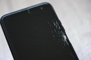 smartphone gebroken glasscherm op houten achtergrond - mobiele telefoon gebroken scherm wacht verander filmscherm in het reparatiewerkplaatsconcept foto