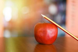 potlood op een appel op de tafel in de bibliotheek - onderwijs leren op houten bureau en wazige boekenplank kamer achtergrond foto